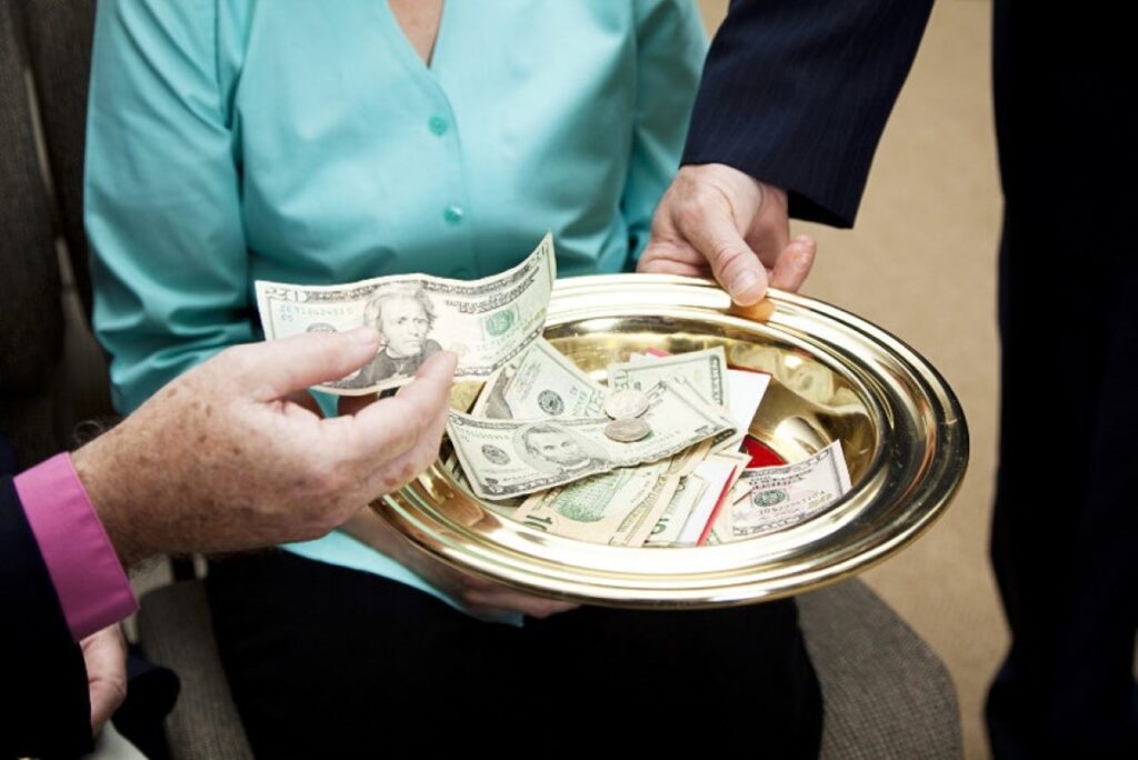 Cash offering plate being passed around and a person is placing cash bills into the plate. 