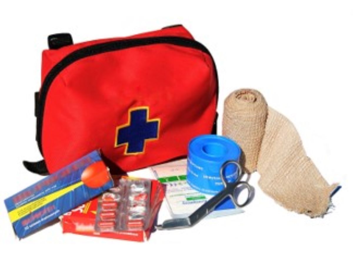 Red medical bag with a black first aid plus insignia sewn on the red bag. Medical supplies that would be  stored inside the first aid bag, including gauze, bandages, scissors and more. are displayed in front of the first aid bag. This picture relates to the sub topic discussed, Medical Emergencies are Safety Issues.