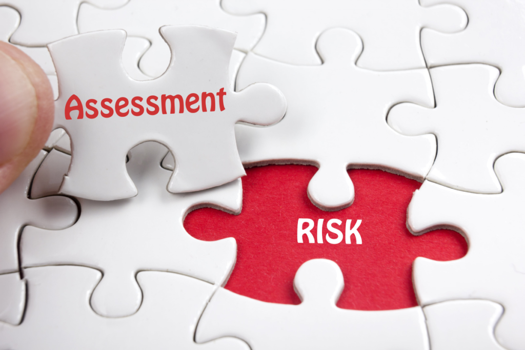 Blank white puzzle together except for 1 piece. The puzzle is sitting on a red paper with the RISK in white lettering. The last white puzzle piece has the word Assessment in Red lettering.